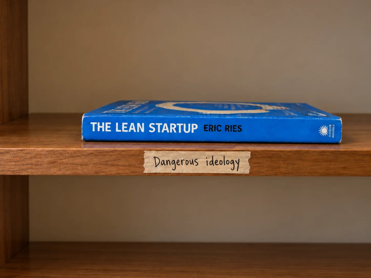 The Lean Startup by Eric Ries lying on a wooden shelf, above a strip of tape that reads “Dangerous ideology”